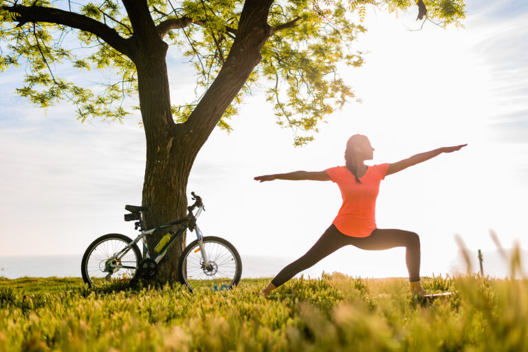slim beautiful woman silhouette doing sports in morning in park doing yoga on mat in colorful fitness outfit in nature, smiling happy healthy lifestyle, calm meditation, bicycle on background